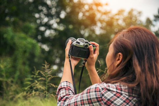 Asian Women with vintage film camera take a photo. Smiling female photographer look at photo from professional camera outdoor. Young woman shooting photo in green nature park. Beautiful woman hobby