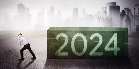 Caucasian businessman pulling a heavy 2024 new year boulder with cityscape background