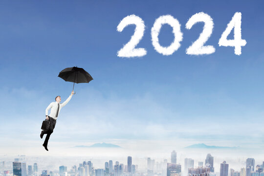 Young caucasian businessman holding an umbrella while flying in the blue sky reaching number 2024