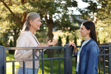 Friendly relationship with neighbours. Happy women talking near fence outdoors