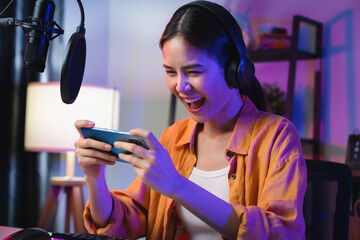 Excited Young Asian woman wearing headset and playing online game on smartphone with live...