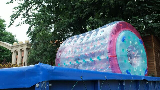 Young girl having fun in zorb cylinder on water surface in amusement park in summer day