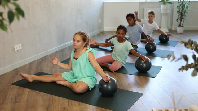 Group of multiethnic kids practicing pilates with soft ball 