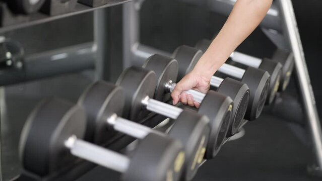Close up of female hand picking dumbbells at gym for weightlifting training