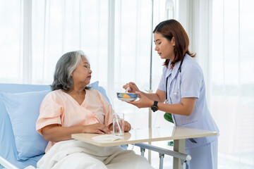 A nurse cares for and feeds an elderly Asian patient who is unable to help himself.