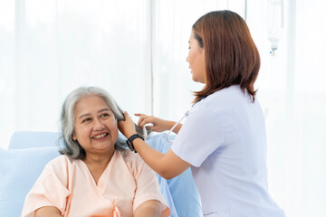 A nurse combs the hair of an elderly Asian patient and offers a pep talk.