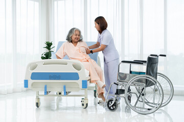A nurse carries an elderly Asian patient from a wheelchair onto a bed after taking him for an x-ray...