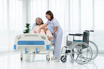 A nurse carries an elderly Asian patient from a wheelchair onto a bed after taking him for an x-ray...