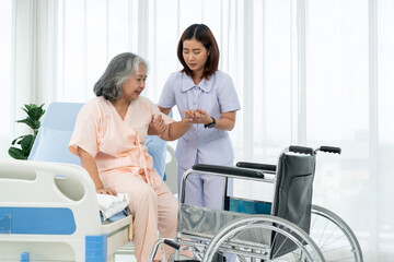 A nurse carries an elderly Asian patient into a wheelchair to take him to get an x-ray of his leg...