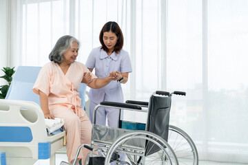 A nurse carries an elderly Asian patient into a wheelchair to take him to get an x-ray of his leg...