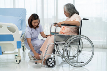 A nurse loads an elderly Asian patient into a wheelchair and makes a footrest ready to take him to...