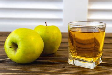 Green apples and glass with apple juice on wooden background