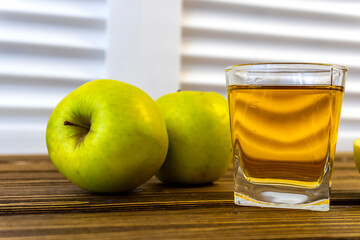 Green apples and glass with apple juice on wooden background