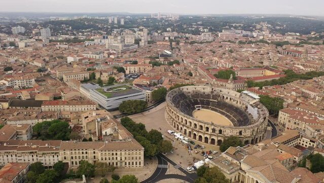 Drone view of ancient Roman amphitheatre Arena of Nimes on background of reddish tiled roofs of residential buildings on summer day, France