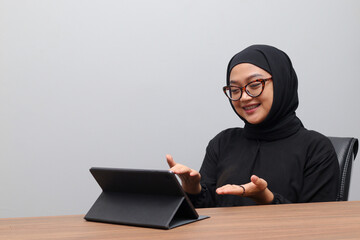 Portrait of attractive Asian hijab woman working on her tablet. Muslim girl doing task in office. Employee and freelance worker concept.