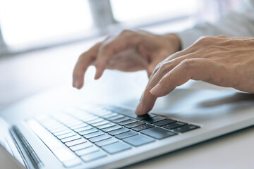 Closeup of businessman's hands typing on a laptop computer for data input and analysis in business performance and investment