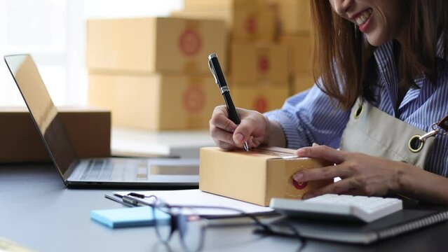 A Female Business Owner Of A Small Online Clothing Store Is Reviewing Internet Orders To Write Notes And Prepare For Delivery.