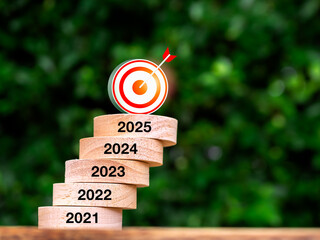 3d target icon on wood block stack growth graph step with year numbers on wooden table. 2021 to...