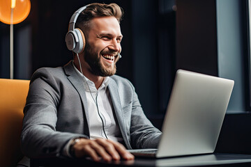 Handsome young man wearing headphones using laptop and smiling while sitting and working in office