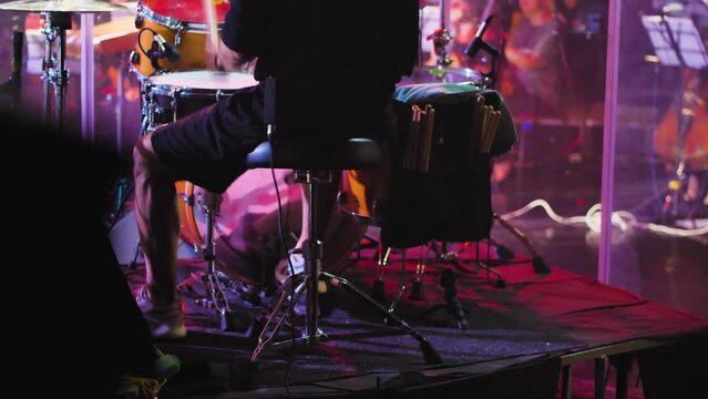 Close-up of drummer's feet pressing pedals of bass drum and hi-hat. Man actively playing drums during performance. Back view. Drummer playing on stage surrounded by lighting effects