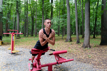 A young man leads a healthy lifestyle and does physical activity on outdoor exercise equipment in a...