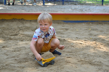 Cute toddler boyl playing in sand on outdoor playground.