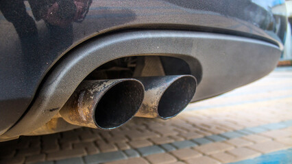 Double turbine exhaust pipe of a black car close-up on multi-colored paving stones