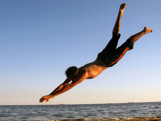 The guy makes a jump forward "fly roll" against the background of the sky and the sea	
