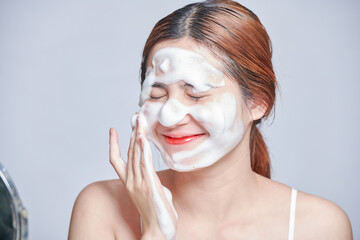 Smiling young woman washing foam face by natural foamy gel. satisfied girl with bare shoulders applying cleansing beauty product on cheeks. personal hygiene, skincare daily routine.