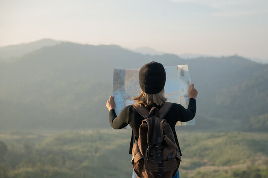 Adventurous girl navigating in with a topographic map in beautiful mountains of thailand. woman wearing hat stand alone and enjoying freedom and calm inspired travelling on background view mockup.