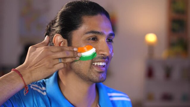 Closeup shot of a man with a tight hair bun painting Tiranga on his face with a wide smile - cricket fan  India fan  sports fan  football fan. Sports lover  patriotism  tricolor tattoo  Indian flag...