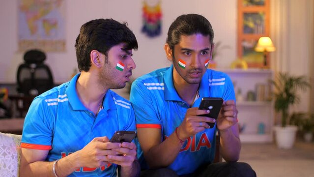 Two young brothers checking the live cricket score - placing online bets  Indian cricket teams  sports app  online gaming addiction . Indian men watching online live cricket match on an app  cricke...