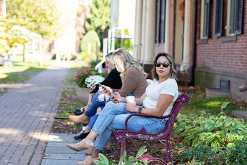 Naklejka premium woman wearing sunglasses holding phone and coffee sitting on a bench