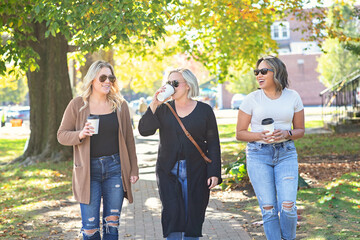 Three women walking down Main Street drinking coffee; friendship