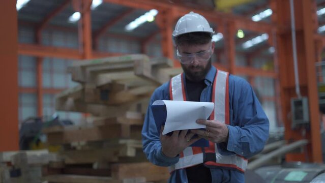 Male worker uses a file to check stock at a factory warehouse. Asian male employee is working in an industrial warehouse. worker wearing a helmet