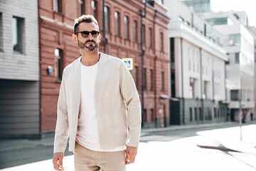 Fototapeta premium Portrait of handsome confident stylish hipster lambersexual model. Sexy modern man dressed in elegant suit. Fashion male posing in the street background in Europe city at sunset. In sunglasses