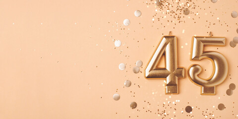 45 years celebration. Greeting banner. Gold candles in the form of number forty five on peach background with confetti. - obrazy, fototapety, plakaty