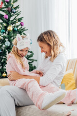Mother hugging cute daughter in pajamas and laughing. Christmas holidays at home. High quality photo