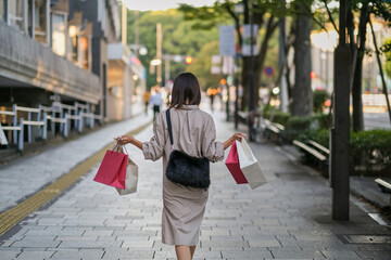 Naklejka premium ショッピングバッグを持って街を歩く女性の後ろ姿