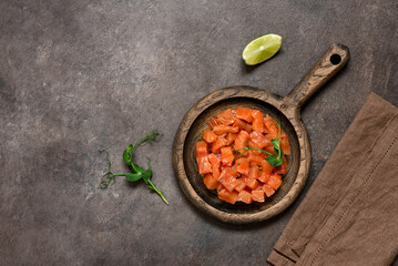 Raw salmon tartare with avocado on a wooden plate, dark rustic background. Top view, flat lay. Vertical