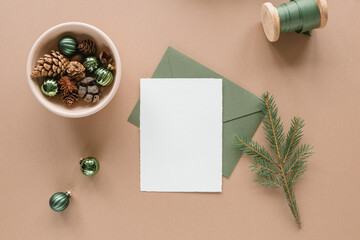 Festive composition of paper card mock up, envelope and Christmas ornaments on beige background.  New Year celebration.
