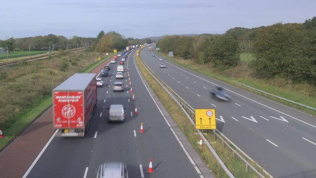 Slow moving traffic on English motorway with train passing on left. Time lapse 15x. M6 motorway, North Lancashire, England, UK.