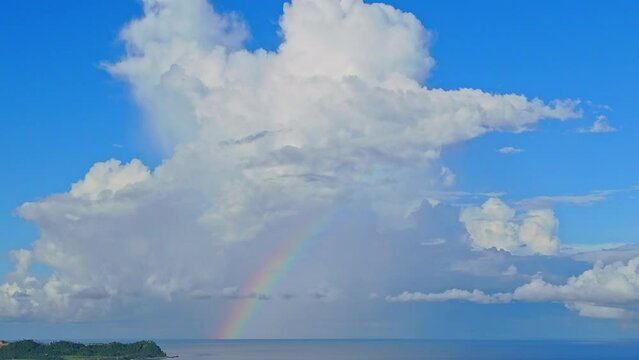 A beautiful rainbow over a calm blue seascape with a large fluffy white cloud towering over it. 