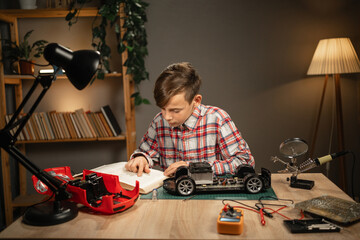 Teen boy repairing a typewriter reads a book using a soldering iron while sitting at home. Child making robot car for a school project in his workshop