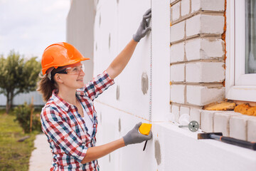 Insulation of the house with polyfoam. The worker is checking with the construction level the accuracy of the installation of polystyrene board on the facade.