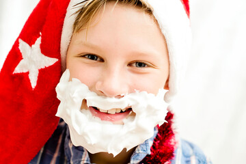 Shaving foam Santa Claus. 10 - year old boy with Christmas hat and beard of aerosol spray cream