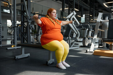 Fototapeta na wymiar Portrait of young overweight woman using dumbbells for working out in gym