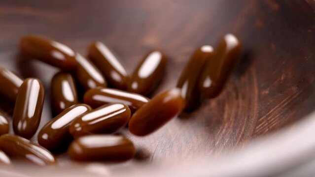 Lecithin supplement soft capsules falling into a dark wooden bowl. Brown nutritious pills. Rotation