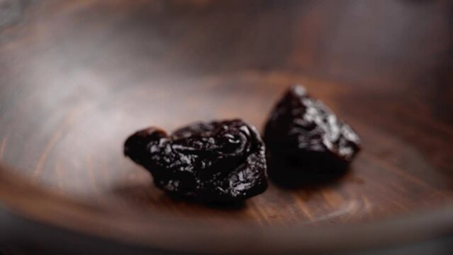 Ripe dried seedless prunes falling into a dark wooden bowl. Dry conserved fruit ingredients close up