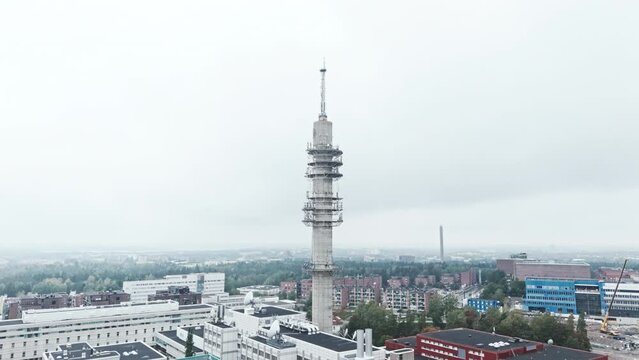 Aerial wide shot of a bleak industrial concrete television and radio link tower in Pasila, Helsinki, Finland on a bright and foggy day. Camera orbiting around, apartment buildings in background.